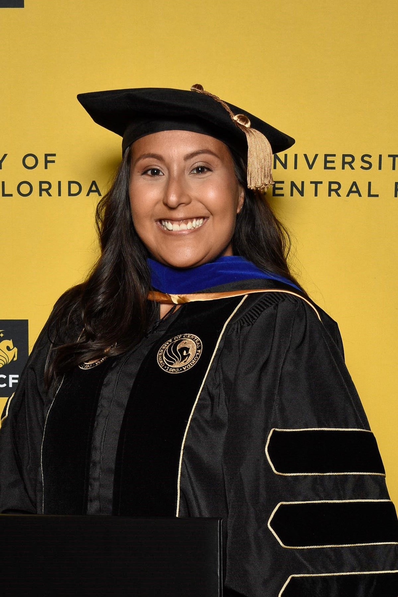 Dr. Ortega in regalia in front of the University of Central Florida backdrop